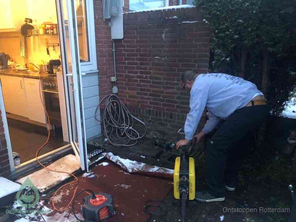 Een monteur werkt buiten bij een open riool-/grondput met een elektrische ontstoppingsmachine om een verborgen afvoerprobleem op te sporen in Rotterdam
