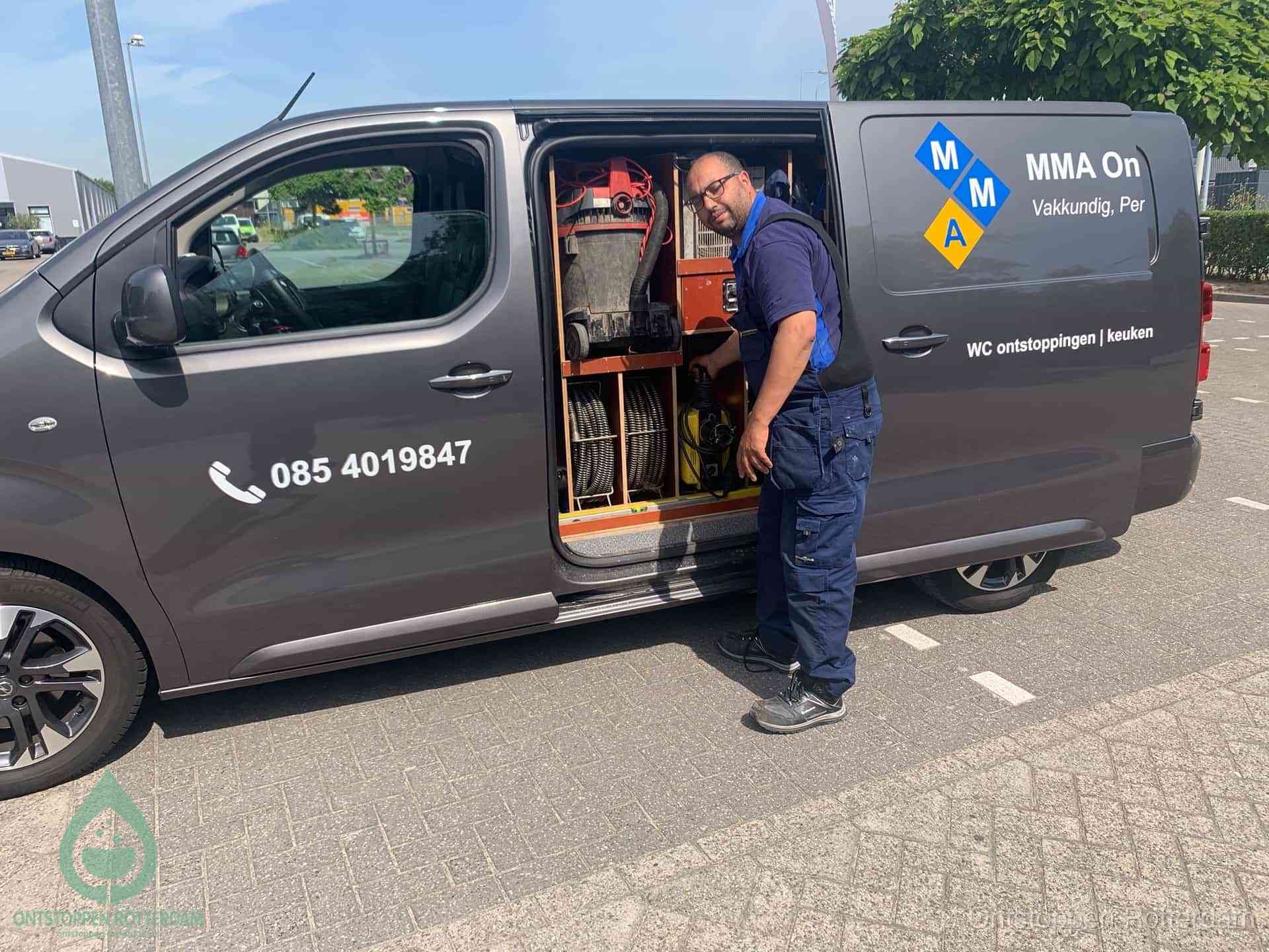 Een monteur bij de open schuifdeur van zijn bedrijfsbus op een parkeerplaats, klaar om de oorzaak van terugkerende afvoerverstoppingen aan te pakken in Rotterdam