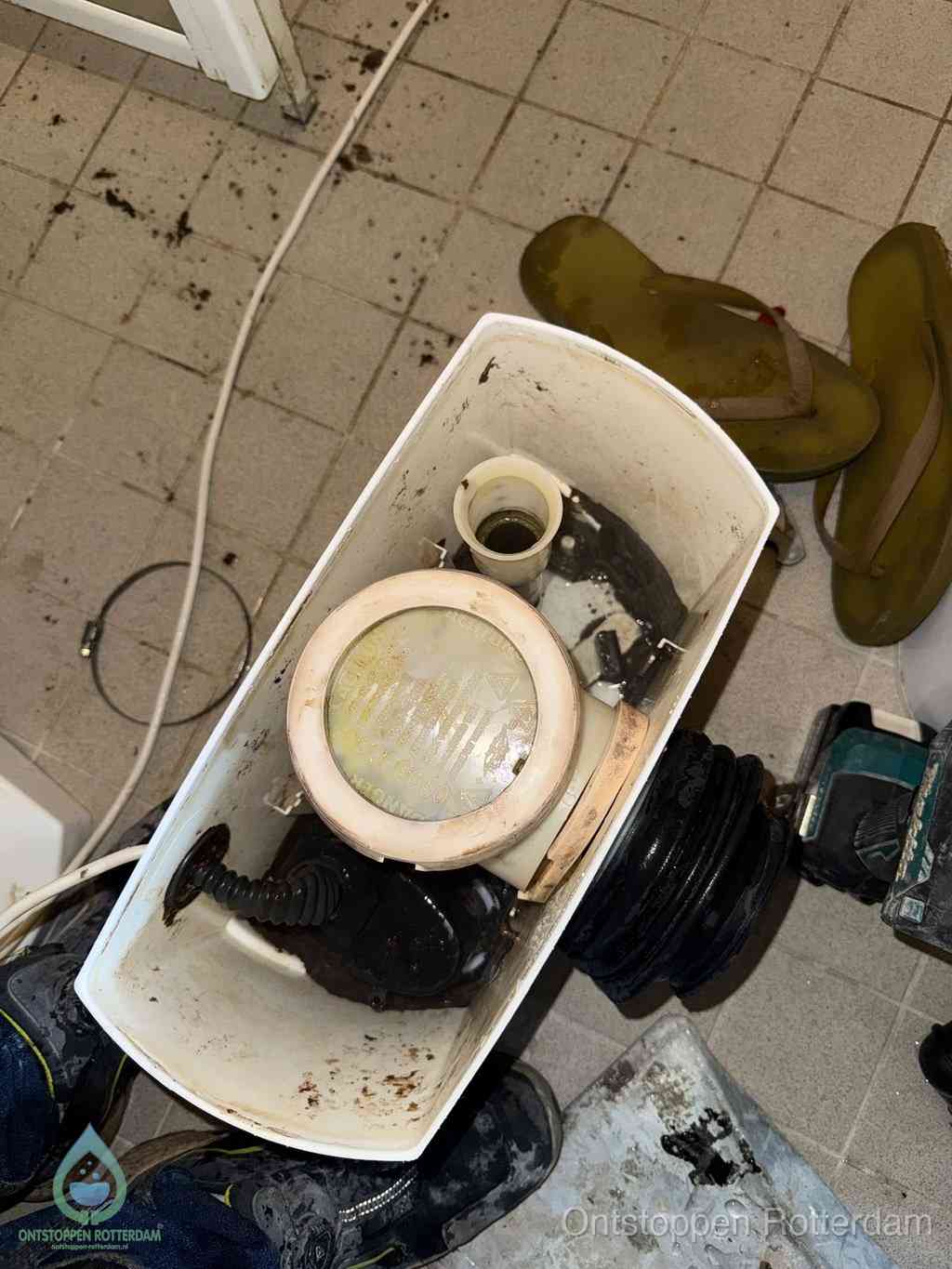 Een gedemonteerde toiletpot op de vloer met ontstoppingsveer en gereedschap ernaast, het verwijderen van een vastzittend voorwerp uit de wc in Rotterdam