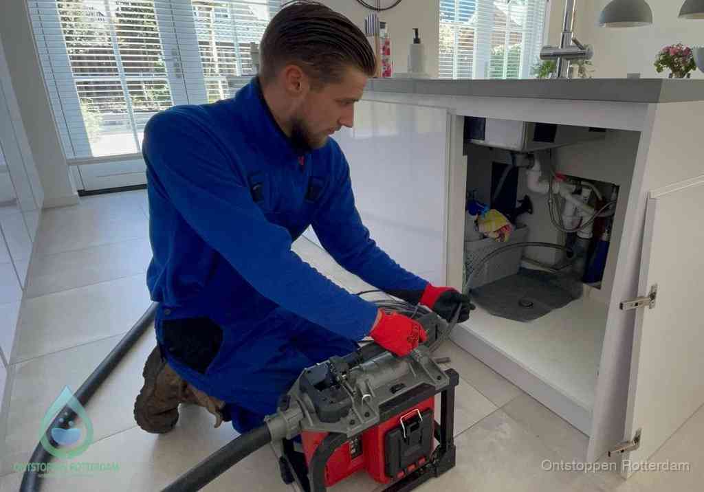 Een monteur voert een professionele elektrische ontstoppingsmachine in de afvoer onder de spoelbak tijdens het gootsteen ontstoppen in Rotterdam