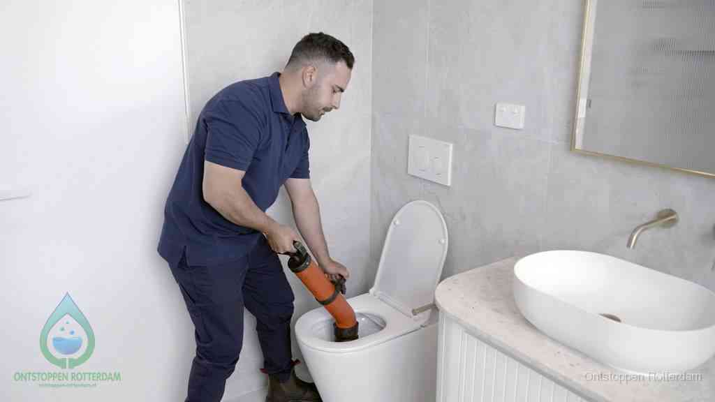 Een man gebruikt een handmatige luchtdruk-ontstopper in een modern betegeld toilet om zelf de wc te ontstoppen in Rotterdam